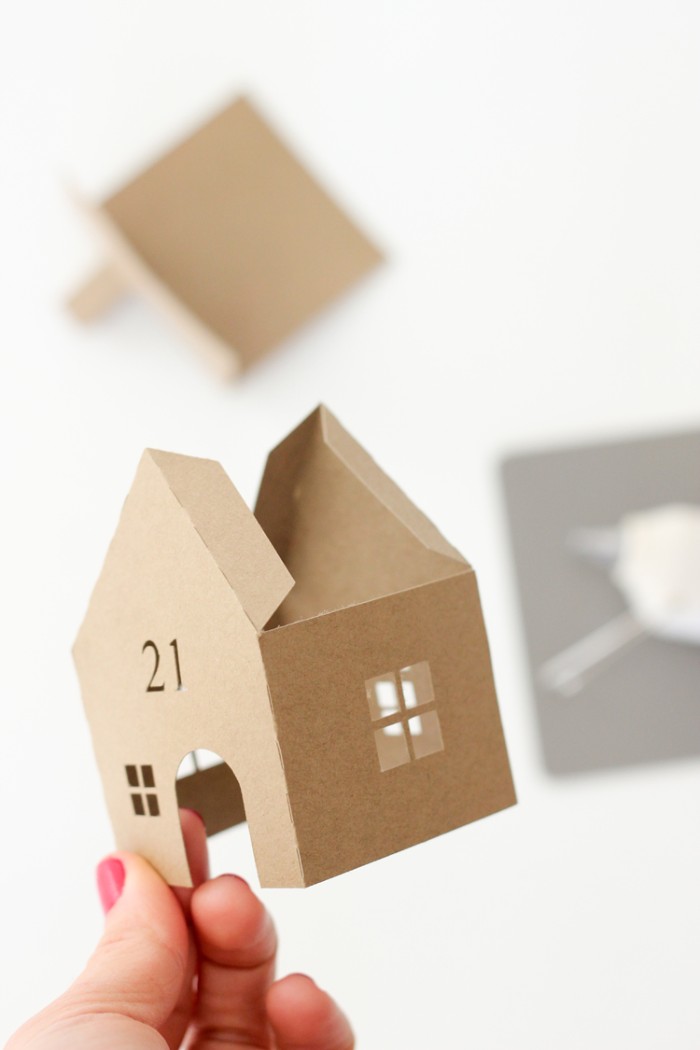 almost finished house, without a roof, made of beige card, with cutout windows, door and the number 21, adult advent calendar idea, held by a hand, with red nail polish