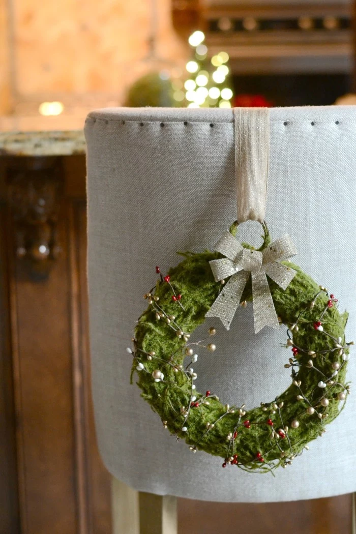 christmas wreath images, green wreath covered by a mossy texture, and decorated with twisted wire, featuring red and white faux berries, hanging on a grey armchair