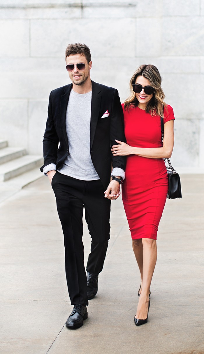red short-sleeved midi dress, worn by a smiling woman, holding the hand of a man, dressed in a smart black suit, with an off-white t-shirt, black tie optional, black shoes and sunglasses