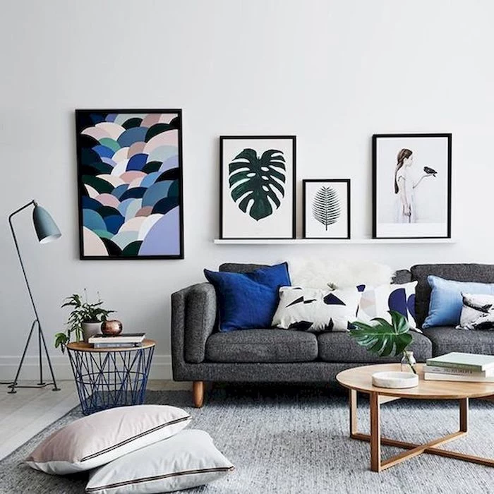 white wall, minimalist paintings, wooden floor with grey carpet, dark grey couch with printed blue and white throw pillows, small wooden coffee table, small living room decorating ideas