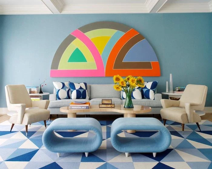 blue wall with a geometrical minimalist painting, blue sofa with blue and white throw pillows, wooden coffee table, white and blue chairs, living room decorating ideas