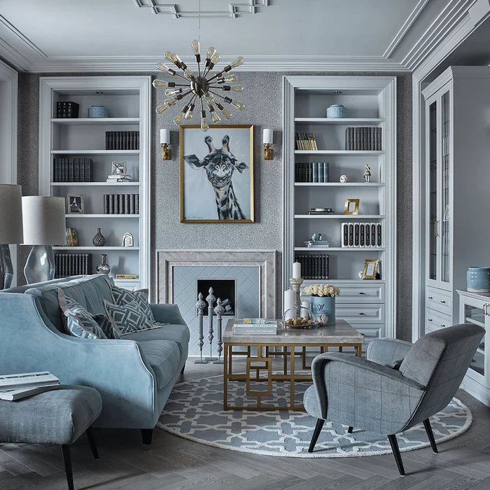 light grey walls, wooden flooring, blue sofa with printed throw pillows, large bookshelves, painting above a fireplace, hanging chandelier, marble coffee table, room ideas