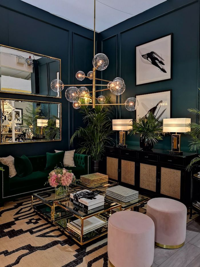 navy walls with mirrors and paintings, dark green sofa with dark green and pink throw pillows, glass and metal coffee table, hanging chandelier, living room decorating ideas