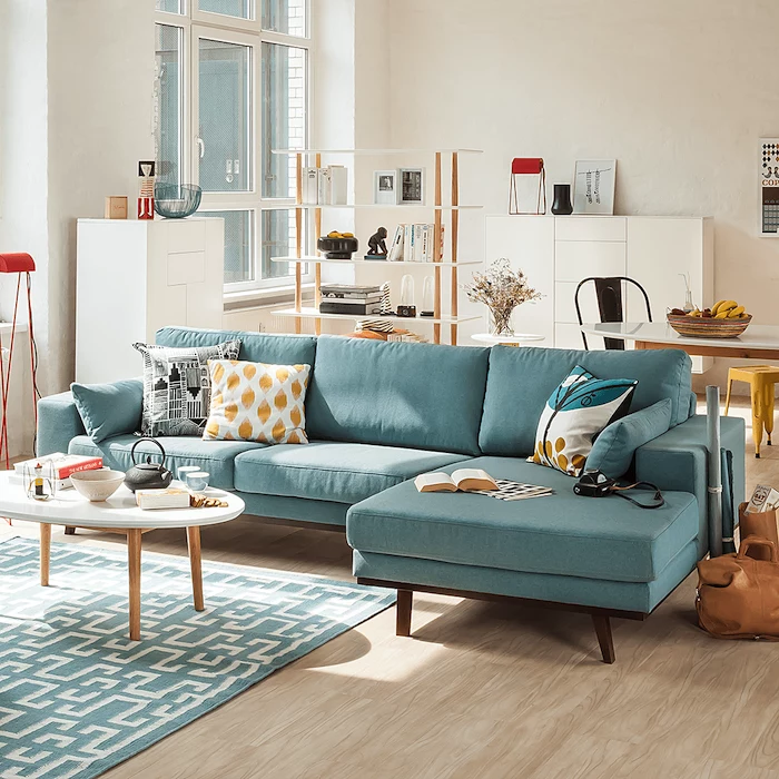 white walls with a wooden floor, blue couch with printed black, blue and yellow throw pillows, blue and white geometrical carpet, small wooden coffee table, living room decorating ideas