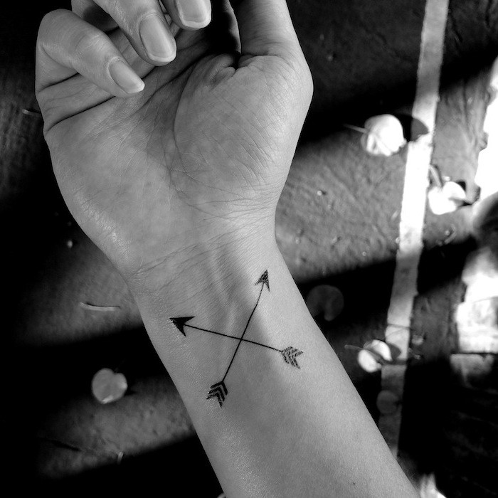 two crossed arrows, small tattoos for girls, tattoo on the wrist, black background