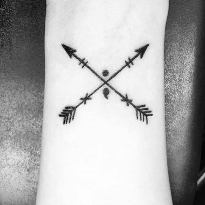 two crossed arrows with a semicolon, tattoo on the wrist, tattoo ideas for women, black background