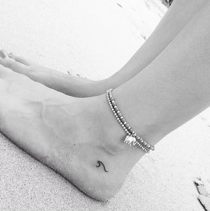 wave tattoo below the ankle, ankle bracelets, tattoos for girls on hand, legs in the sand on the beach