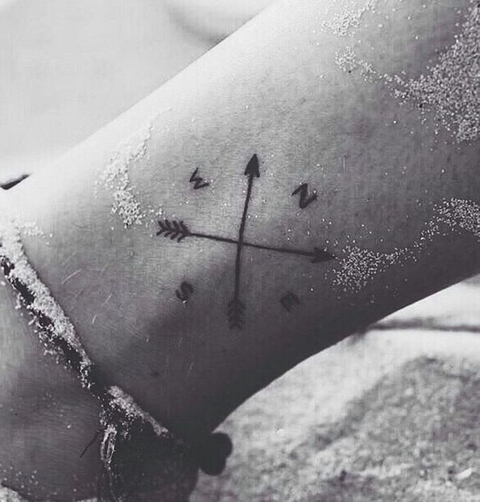 crossed arrows, north west south and east directions, tattoo on the ankle, leg in the sand, meaningful tattoo ideas