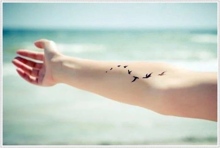 arm in the air, birds tattoo on the forearm, meaningful tattoo ideas, ocean waves in the background