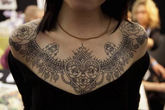 large symmetrical roses tattoo, girl chest tattoos, black top and hair, gold necklace