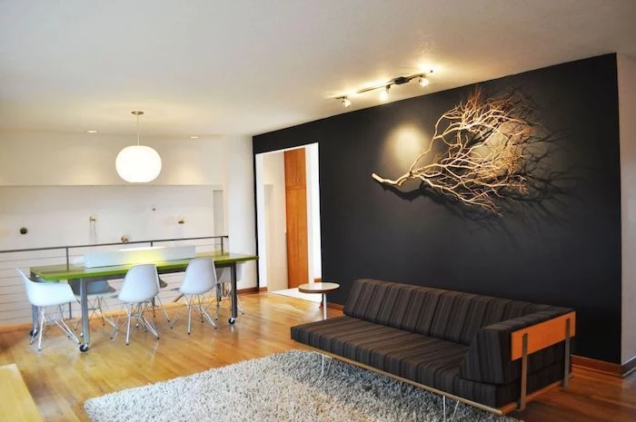 black sofa, black wall with a dried tree branch, wall treatments, white rug, wooden floor