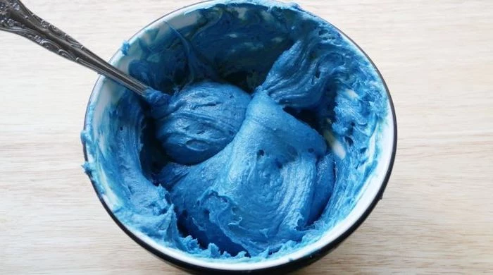 blue cake batter in a bowl, spoon for stirring, unicorn cake, wooden countertop