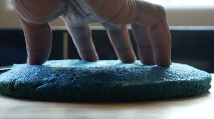 hand pressing blue batter, wooden countertop, unicorn cupcakes