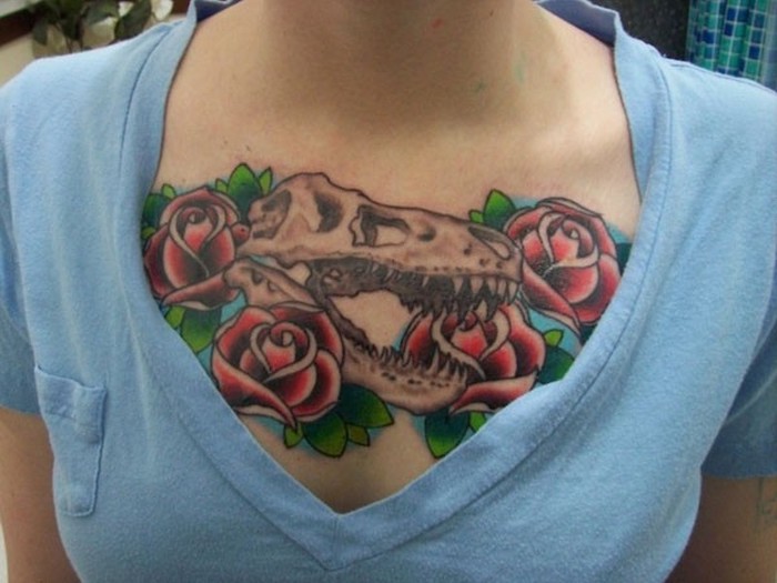 roses and dinosaur skull tattoo, blue top, tattoo between breast, red roses and green leaves, small chest tattoos for females