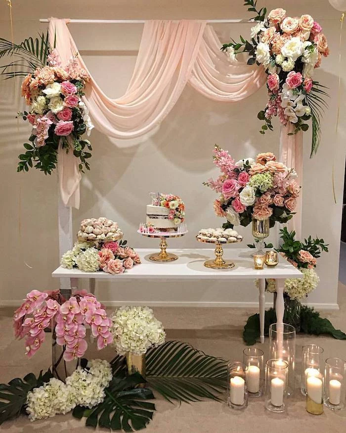 arch with blush tulle and pink white and orange rose flower arrangements, dessert on the table, candles in vases, rustic wedding centrepieces