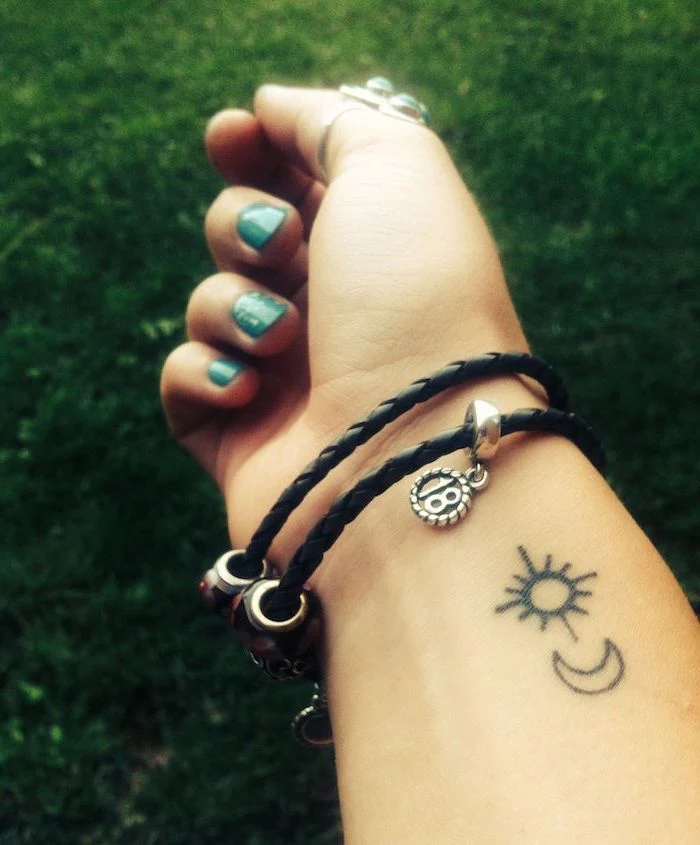 sun and moon tattoo on the wrist, chest tattoos for females, black bracelet with charms, blue nail polish
