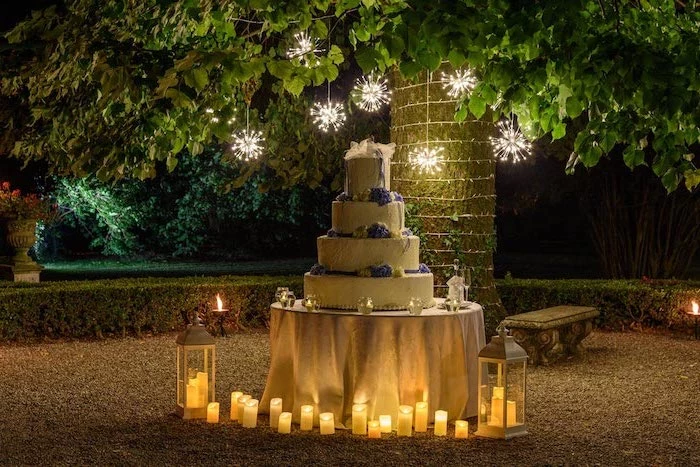 fairy lights on a tree, candles and a lantern, large wedding cake on a table, rustic wedding centrepieces