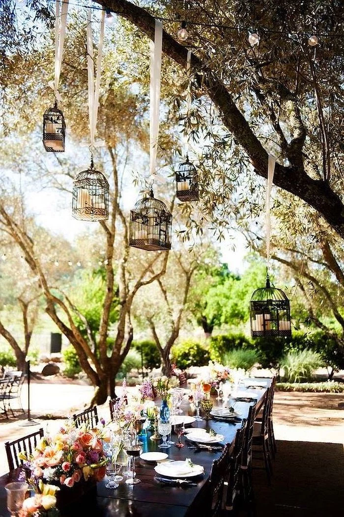 hanging bird cages with candles hanging from the tree, pink white and yellow roses bouquets in vases, fall wedding ideas