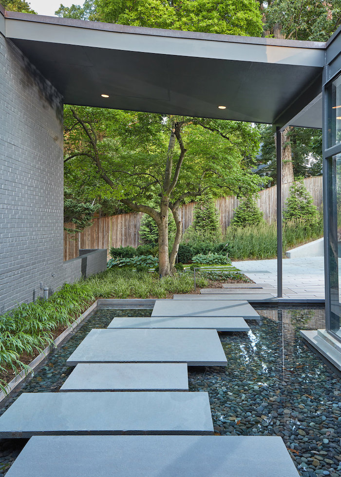 small water pool with rocks in it, geometrical stone tiles pathway, small patches of grass, landscape edging ideas, tall trees