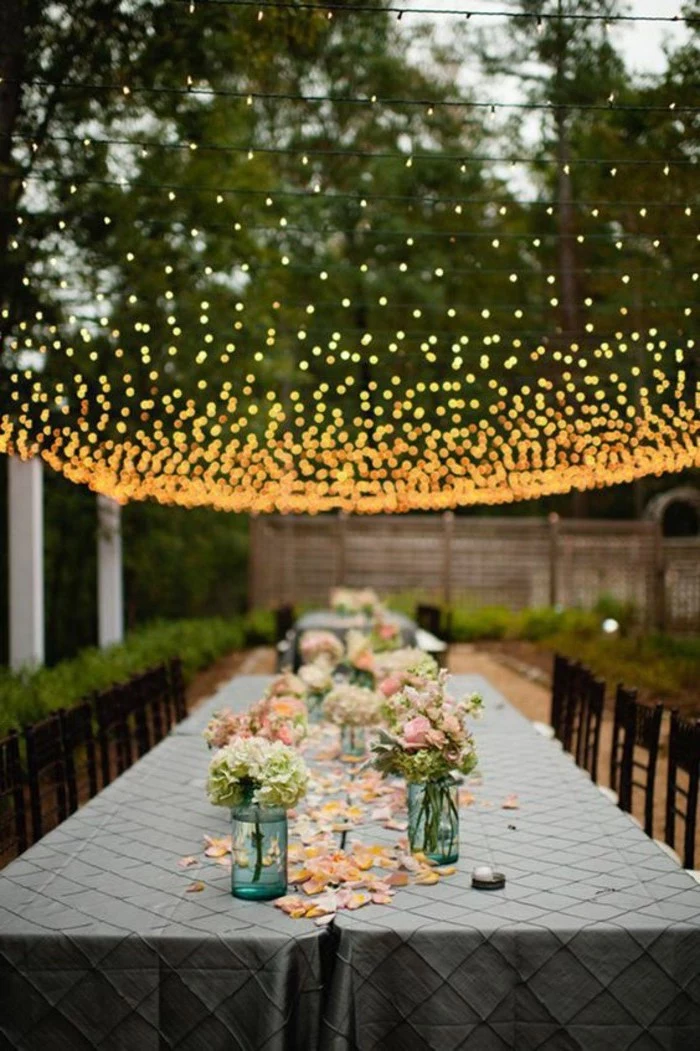hanging fairy lights, pink and yellow flower bouquets in vases, rose petals on the table, wedding reception decorations