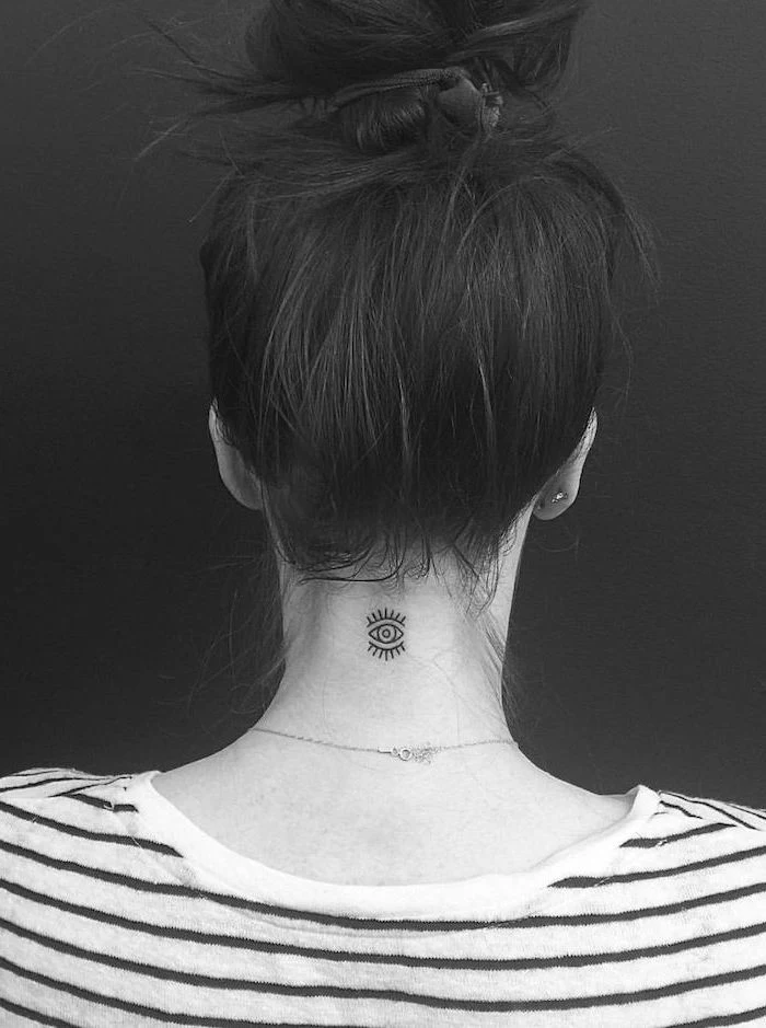 tattoos for women with a meaning, black hair in a bun, evil eye tattoo on the neck, black and white striped shirt