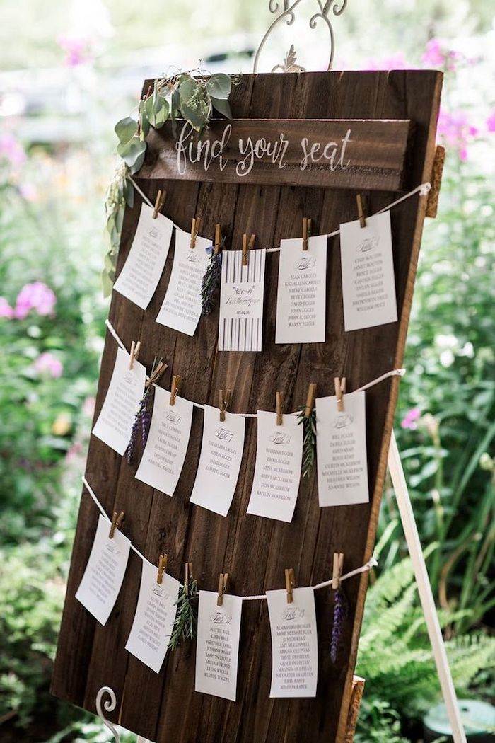 wooden seating chart, papers pinned with pins, greenery in the background, wedding table decoration ideas