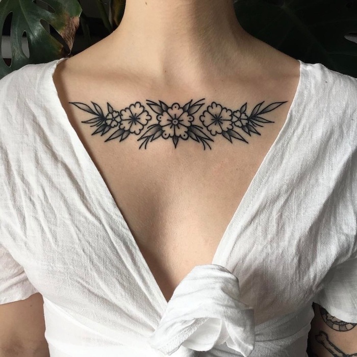 chest tattoo ideas, white shirt, flowers and leaves tattoo, palm leaves in the background, tattoo designs for womens chest