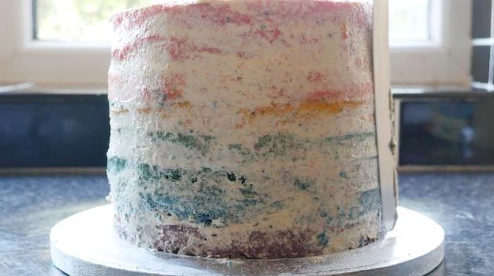 frosting spread around the cake, silver cake stand, unicorn birthday cake, blue countertop