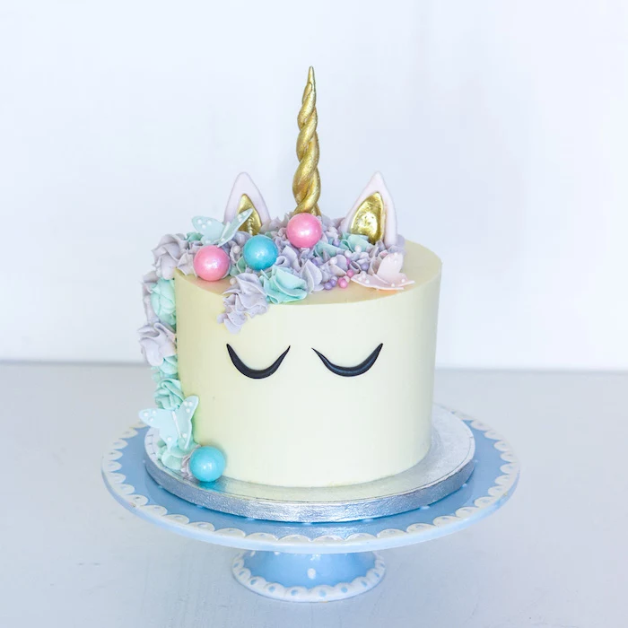 rainbow unicorn cake, blue cake stand, purple and blue roses on white fondant, gold horn and ears