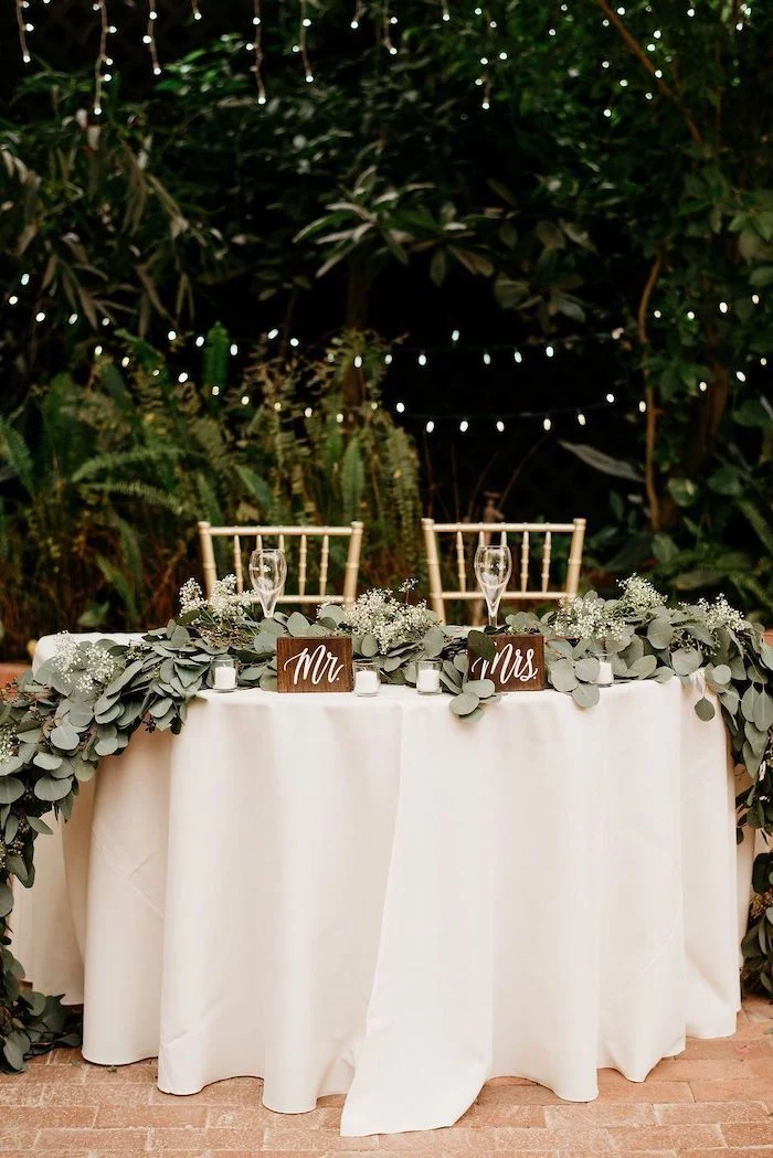 mr and mrs wooden signs, fairy lights and trees in the background, green leaves arrangement on the table, wedding ideas for summer