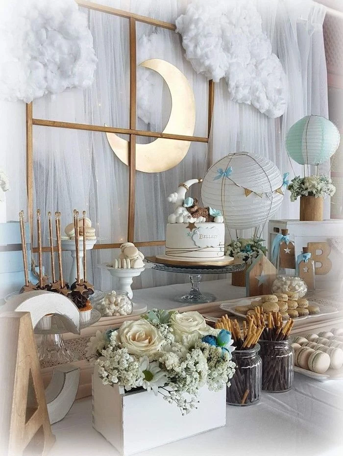 white tulle with fairy lights, baby shower themes for boys, flowers in a wooden crate, cake macaroons and cake pops on the table
