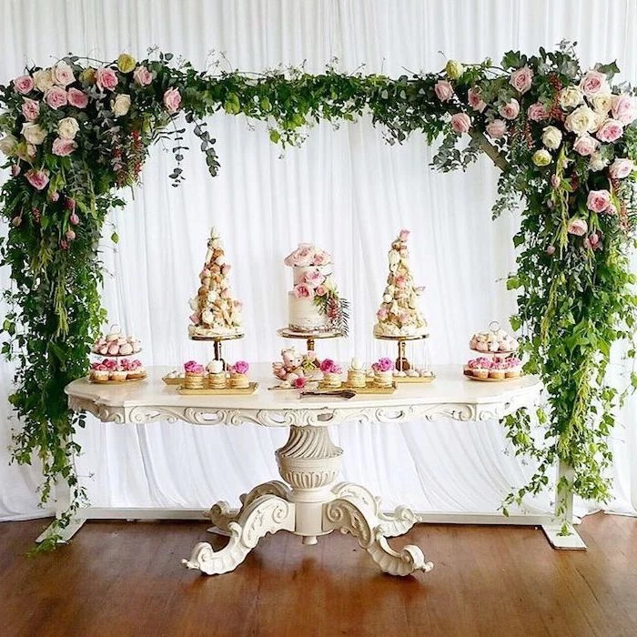 pink white and yellow flower arch, white antique table, cake and macaroon dessert on the table, wedding table decorations