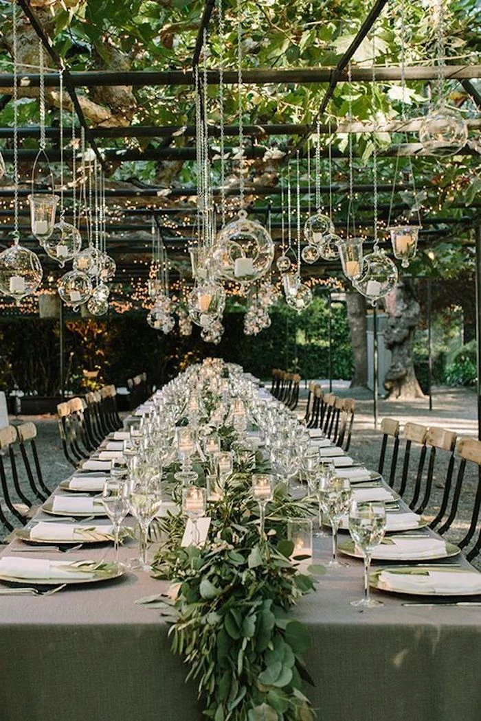 hanging candles from the ceiling, green flower arrangement on the table, dinner sets on the table, wedding reception decorations
