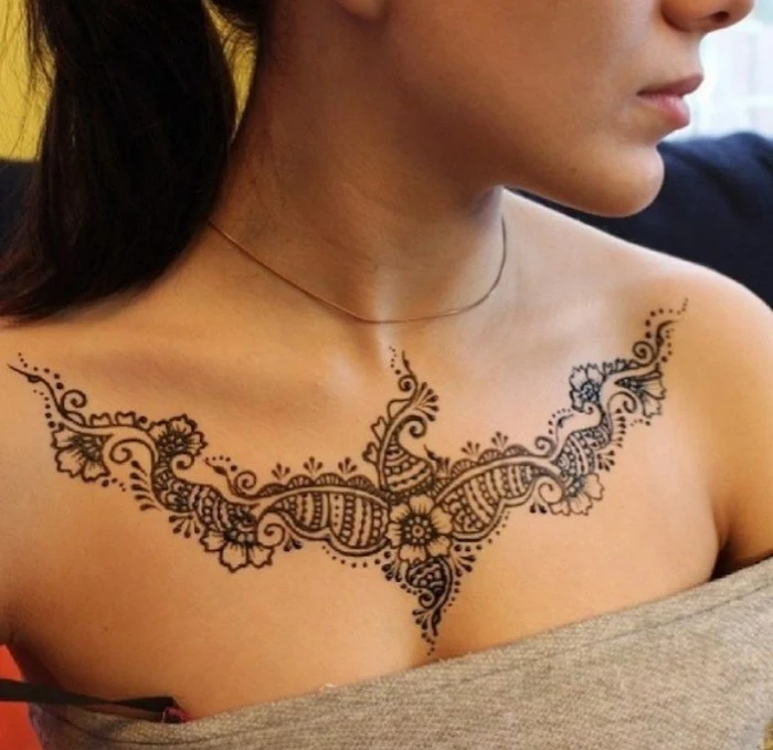 grey top, rose chest tattoo, black hair in a ponytail, symmetrical flowers tattoo, gold necklace, tattoo designs for womens chest
