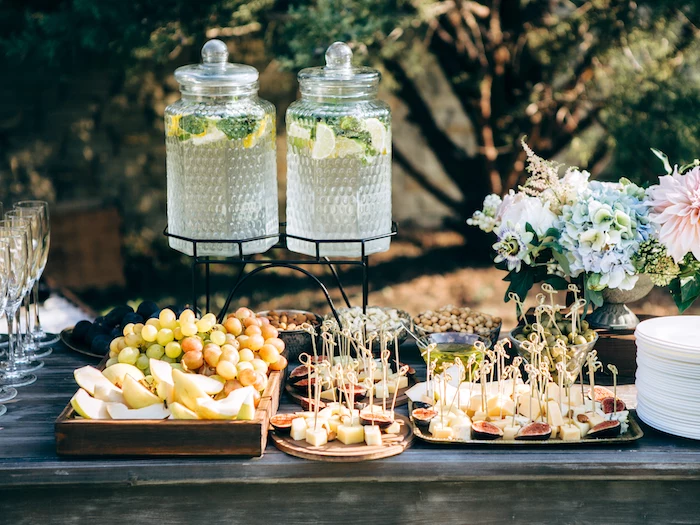 lemonade jars on a stand, grapes and apples in a tray, small bites on trays, flower bouquet in a vase, wedding table decorations
