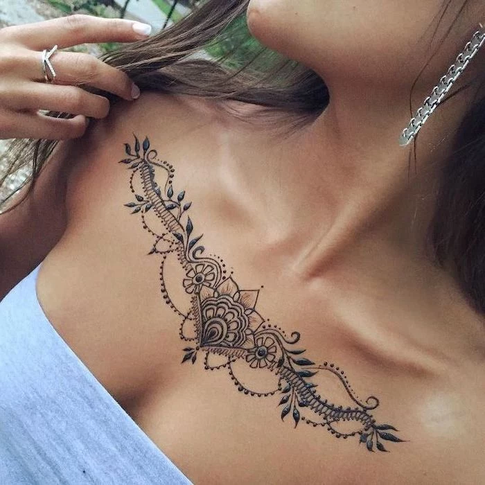 grey top, symmetrical lotus tattoo, tribal chest tattoos, ring and earrings, long brown hair