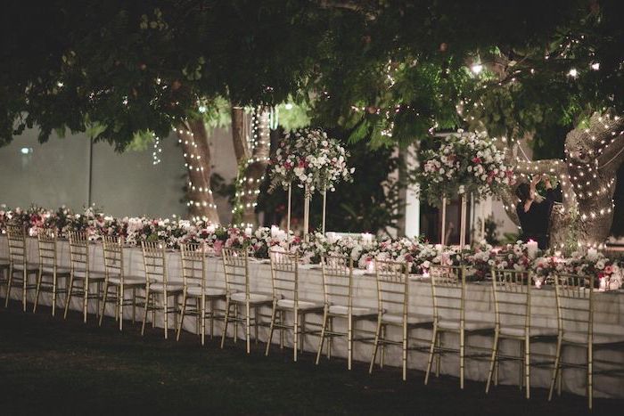white and pink roses flower arrangement on the table, string lights on the trees, wedding decor