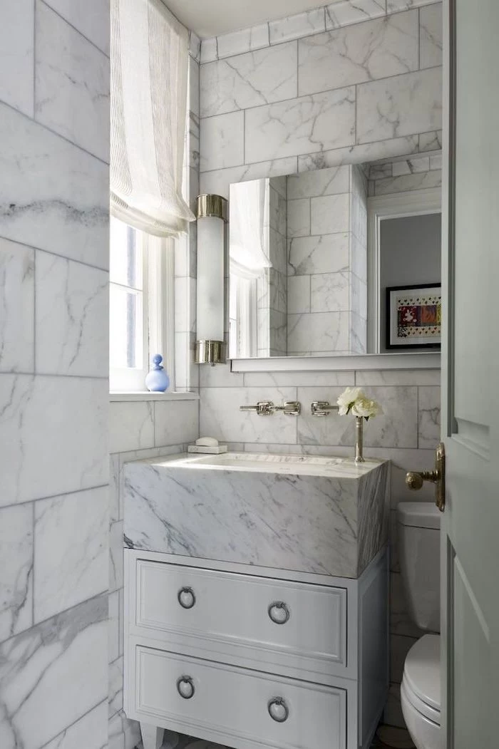 marble tiled walls and sink, white drawers under the sink, large mirror, small bathroom layout