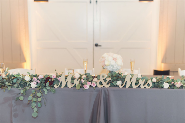 mr and mrs wooden sign, pink and white flower arrangement on the table, white roses bouquet in a vase, wedding table settings