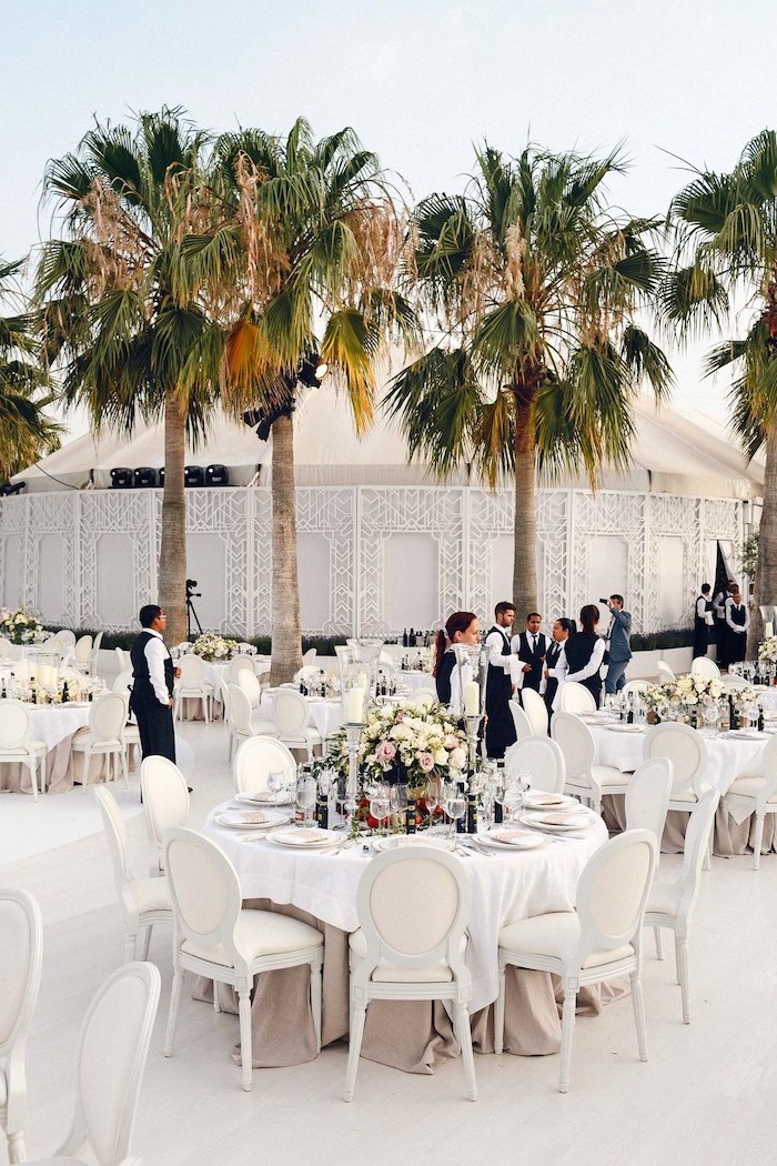 big palm trees, white round tables, yellow and pink roses bouquets, wedding ceremony decorations
