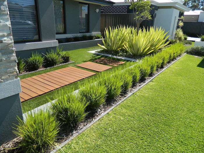 patch of grass, small backyard landscaping ideas, wooden pathway, small symmetrical bushes, 