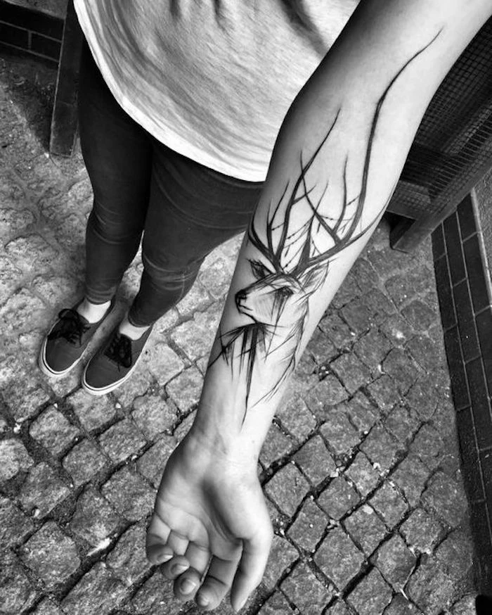large stag forearm tattoo, small tattoos with meaning, paved path, black jeans and shoes, unique hidden meaning tattoos