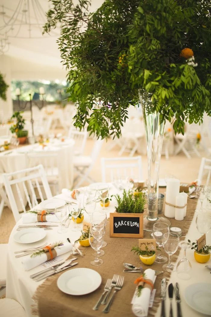 green leaves flower arrangements in a high vase, wooden barcelona sign on the table, wedding ceremony decorations