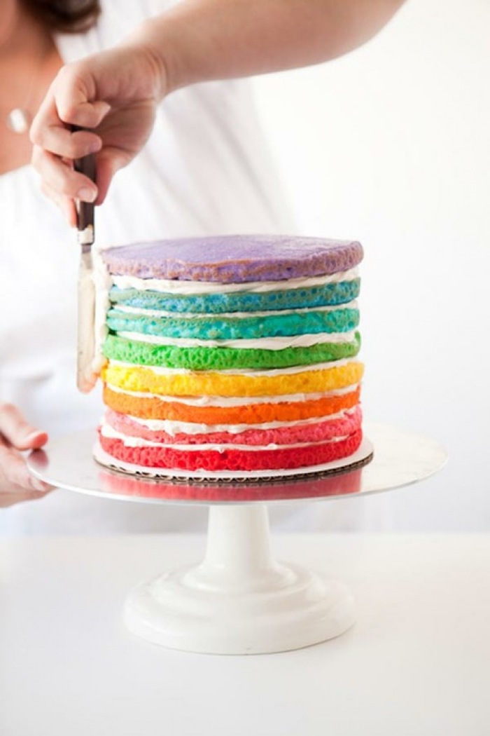 white cake stand, unicorn birthday cake, rainbow coloured cake layers, frosting spread with a spatula