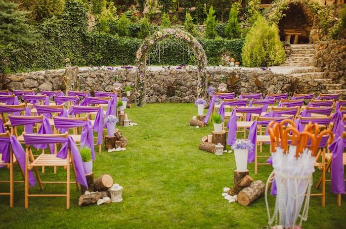 arch made of pink flowers, wooden chairs with purple bows, wood along the aisle, rustic wedding ideas