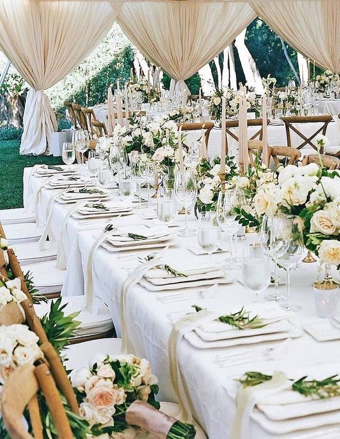 white roses bouquets in vases on the table and on the chairs, candles in candelabrums, ceiling hanging decor