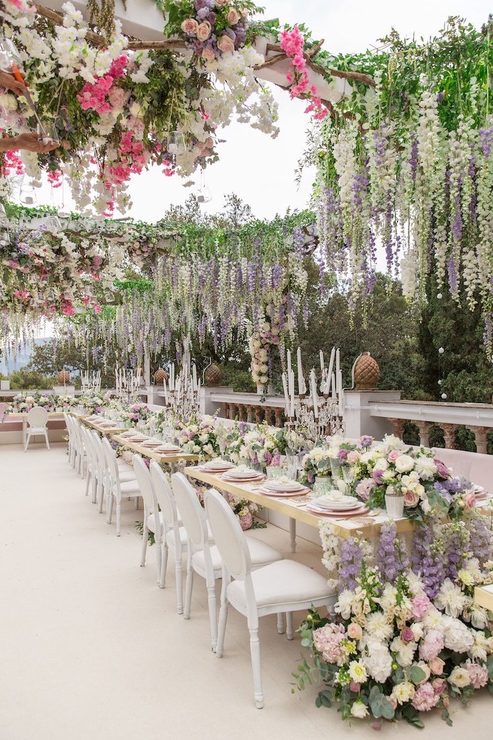 hanging white pink and purple flower arrangements from the ceiling, candles in candelabrums on the table, ceiling hanging decor