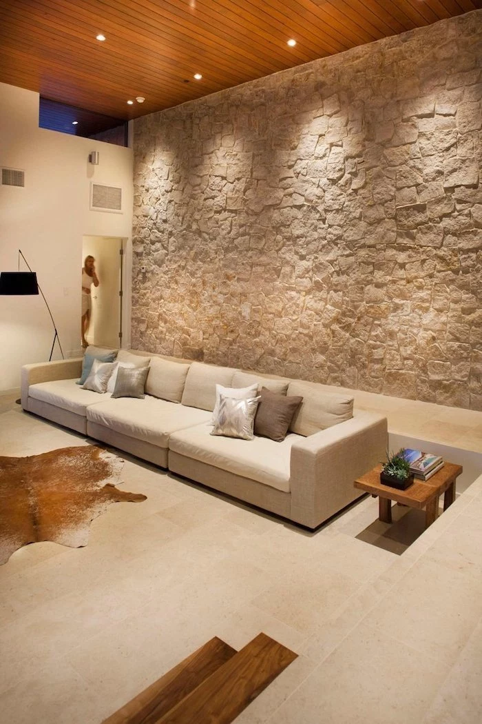 stone wall, large white sofa, small wooden side table, wooden ceiling, feature wall