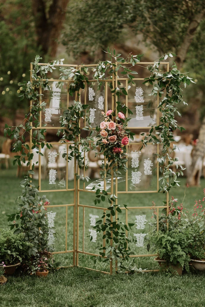 glass geometrical seating chart, hanging roses and leaves, trees in the background, wedding table decoration ideas