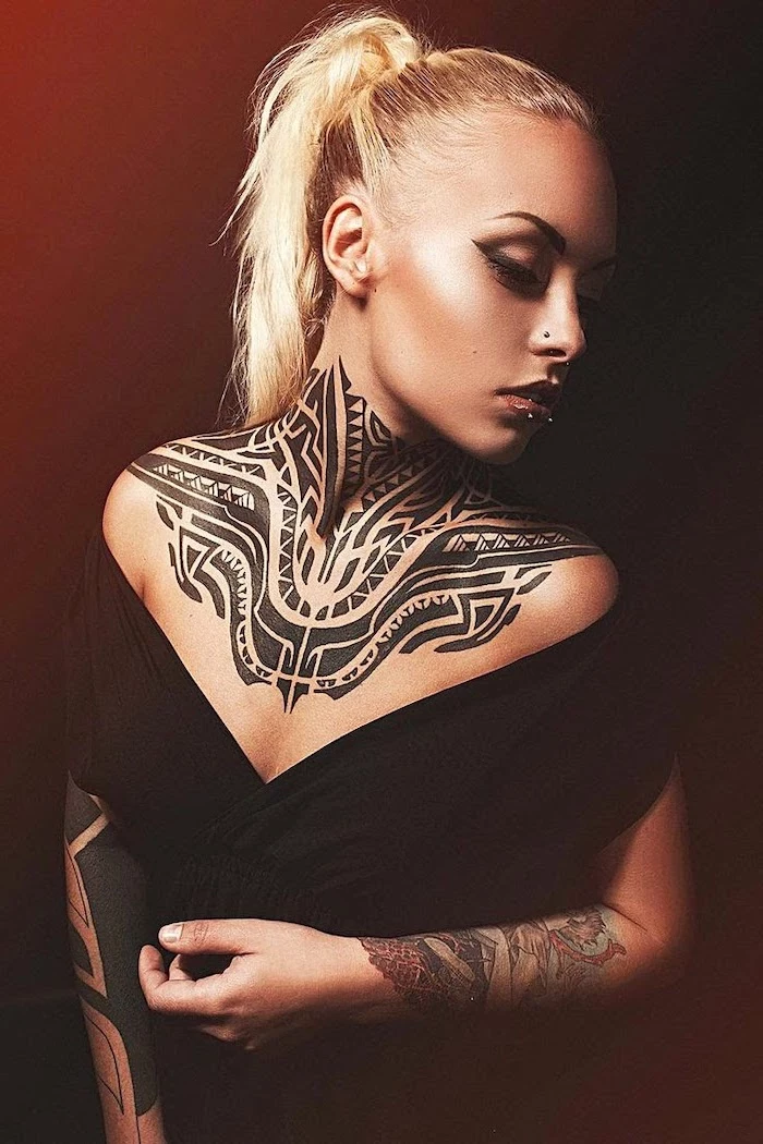 blonde hair in a ponytail, chest tattoos for females, tribal tattoo on the neck chest and hand, black top